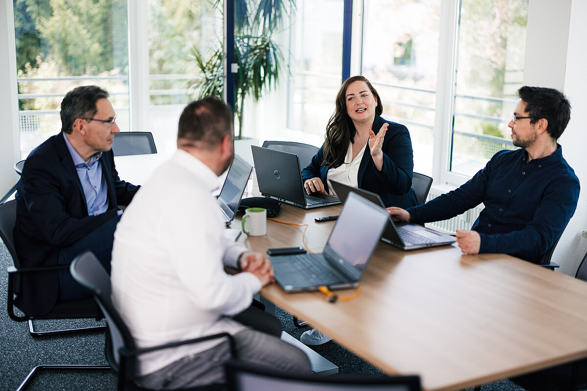 Teammeeting im Büro: Vier Personen diskutieren am Tisch mit Laptops, Fokus auf Zusammenarbeit und Austausch.